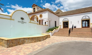 A building with a stone fountain, a staircase, and a sign reading 'The San Roque Club'.
