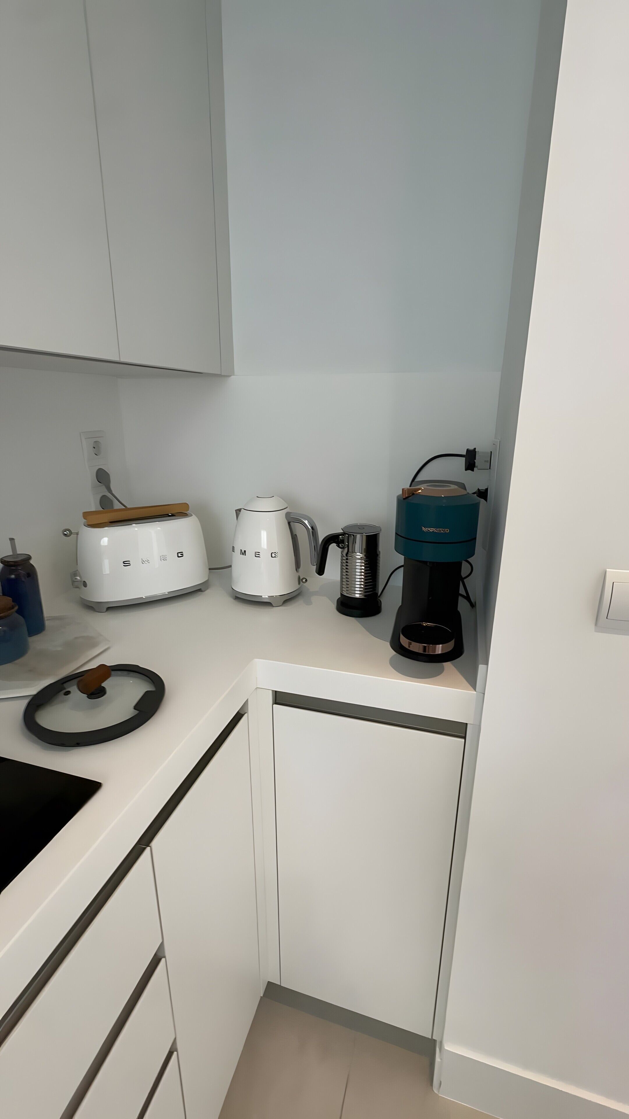 A compact kitchen with white cabinets, a toaster, a kettle, and a coffee maker.