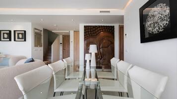 A modern dining area with a glass table and white chairs, a wooden door with a decorative panel, and a framed artwork above the door.