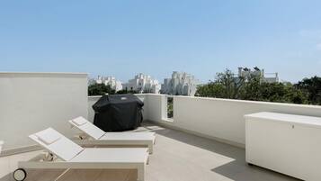 Una terraza en la azotea con sillones de descanso, una parrilla y vistas panorámicas de la ciudad.