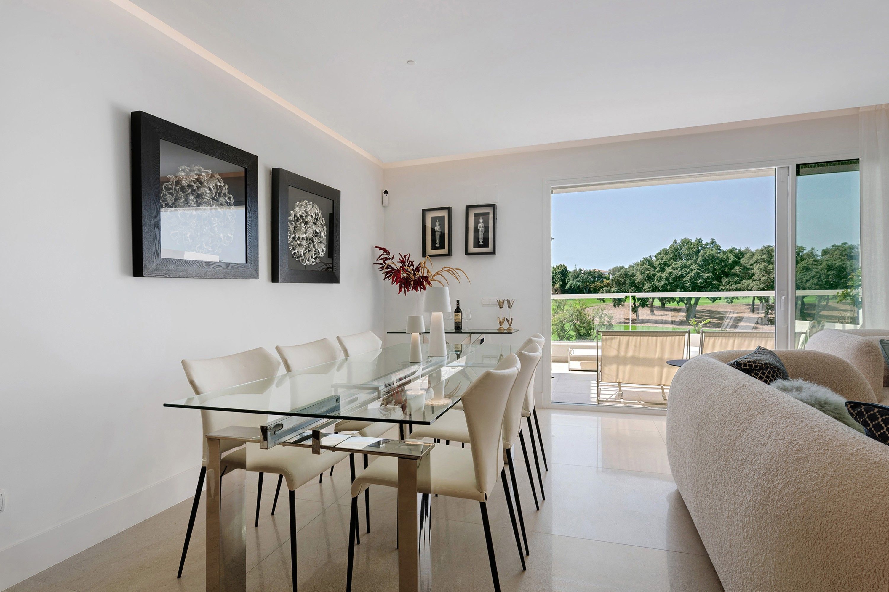 Un comedor moderno con una mesa y sillas de vidrio, un sofá y obras de arte en las paredes.