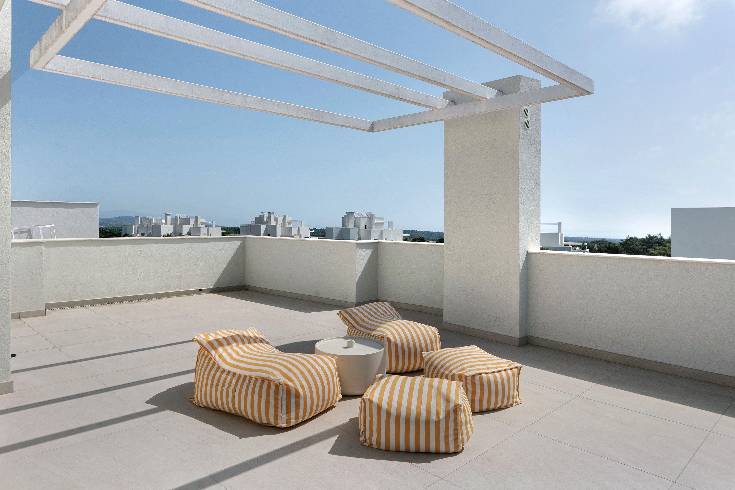 Una terraza en la azotea con una pérgola blanca, cojines a rayas y vistas de la ciudad.