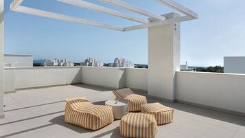 Una terraza en la azotea con una pérgola blanca, cojines a rayas y vistas de la ciudad.