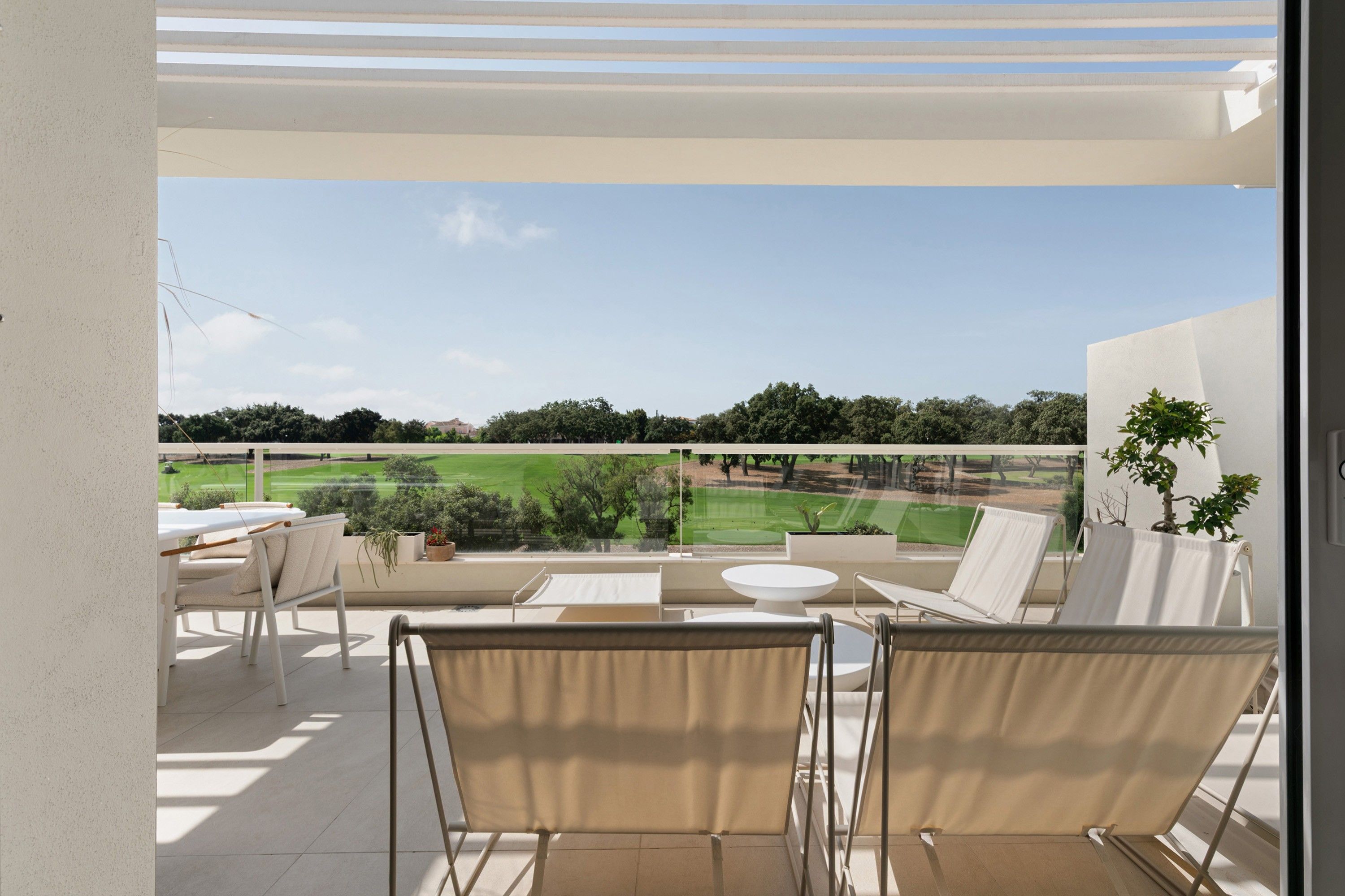 Un balcón con vista a un campo de golf, mobiliario exterior y una planta en maceta.