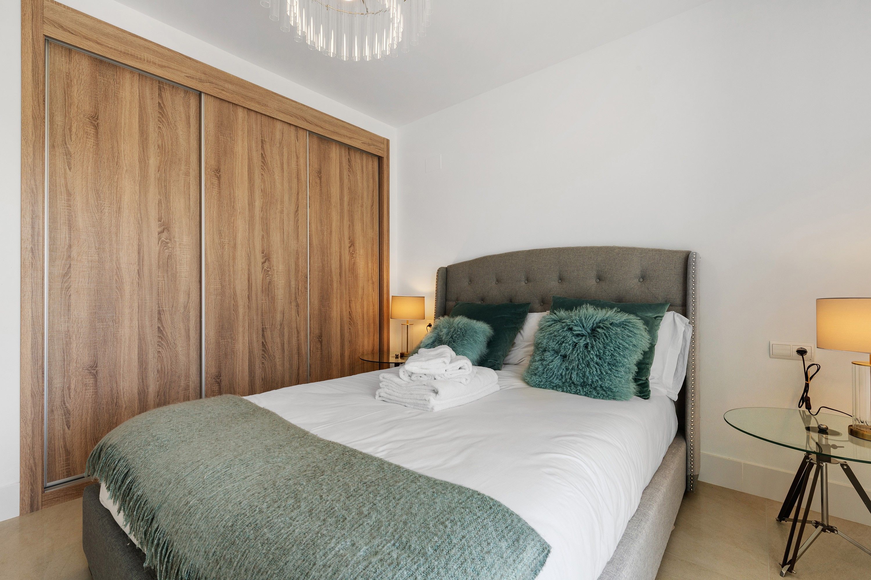 Een slaapkamer met een bed, een glazen tafel, een lamp en een kledingkast.