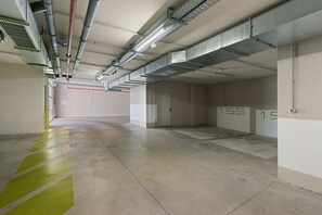 A clean, empty parking garage with concrete floors and walls, ventilation ducts, and numbered parking spaces.