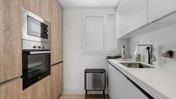 A modern kitchen with stainless steel appliances, a wooden cabinet, a white countertop, and a stainless steel trash bin.