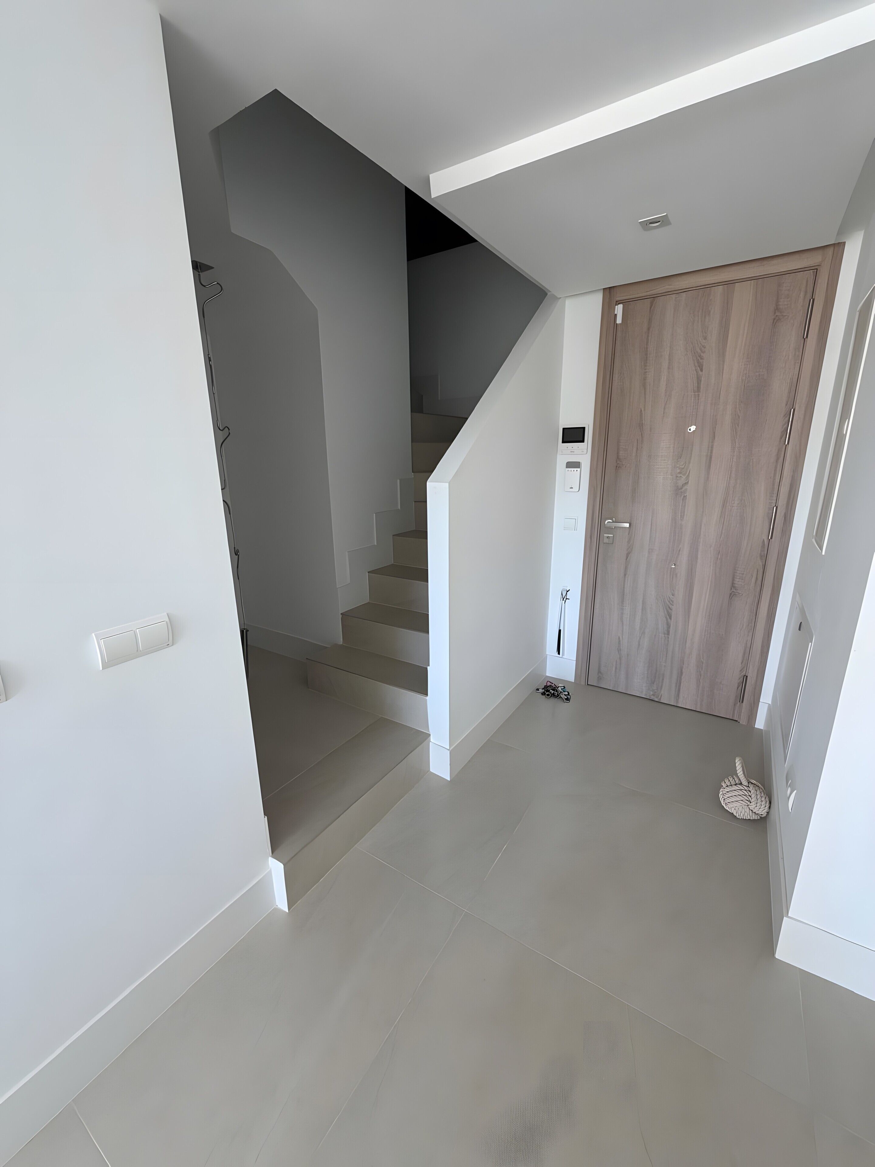 A modern interior with a staircase, a wooden door, and a light switch on the wall.
