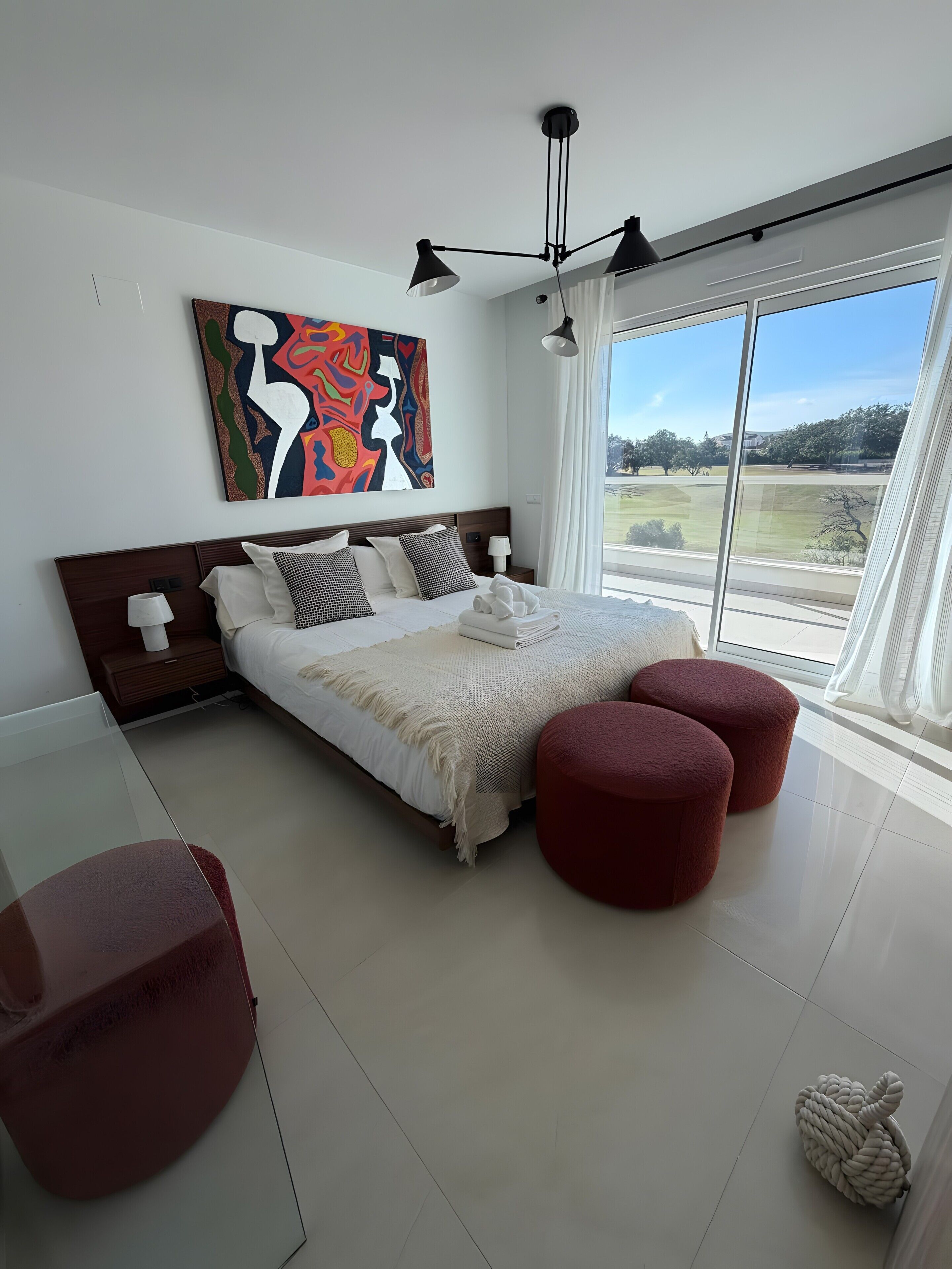 Un dormitorio moderno con una cama grande, vistas al exterior y una obra de arte original en la pared.