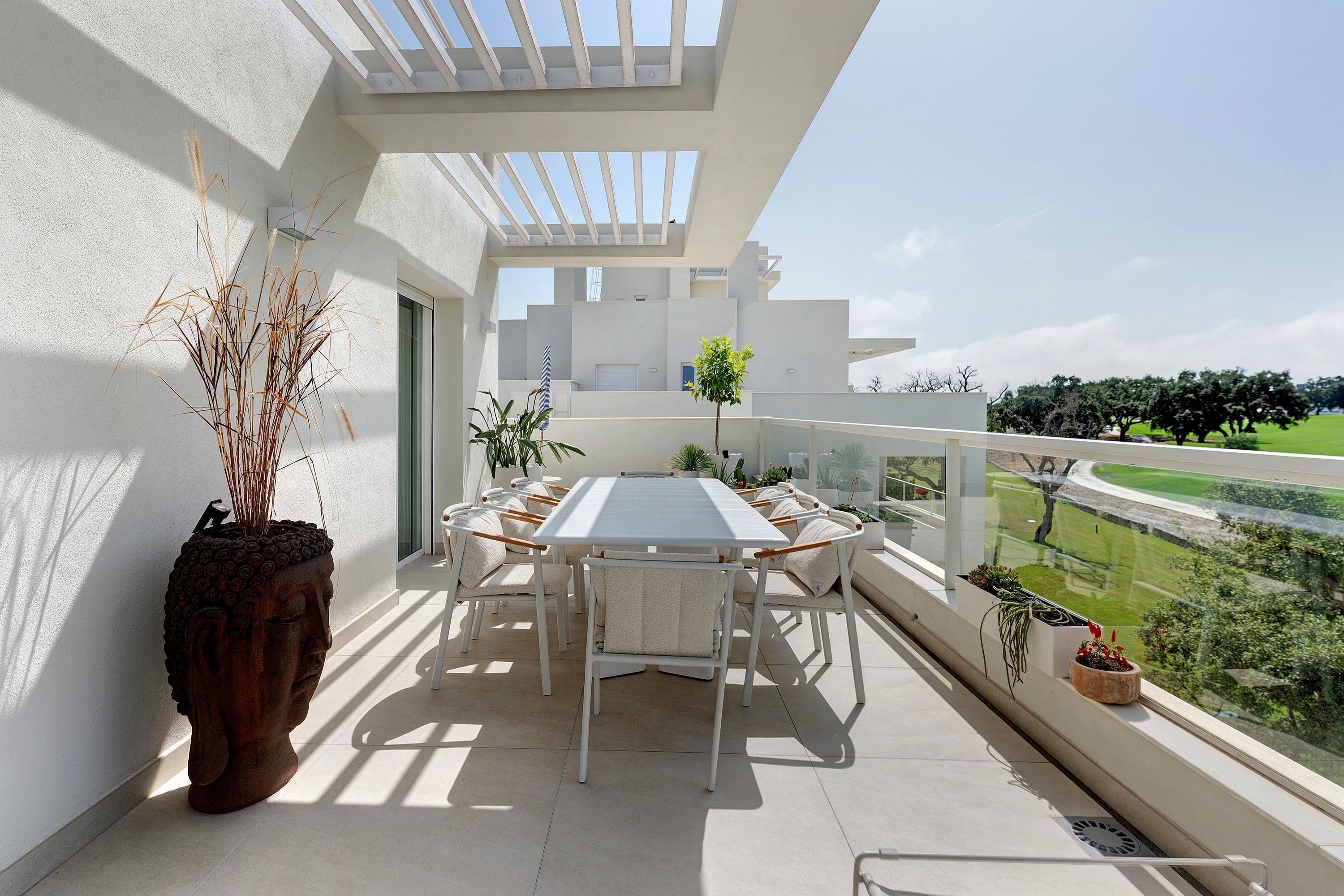 Un balcón con mesa y sillas, plantas en macetas y vistas a un paisaje verde.