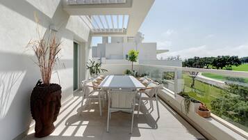 Un balcón con mesa y sillas, plantas en macetas y vistas a un paisaje verde.