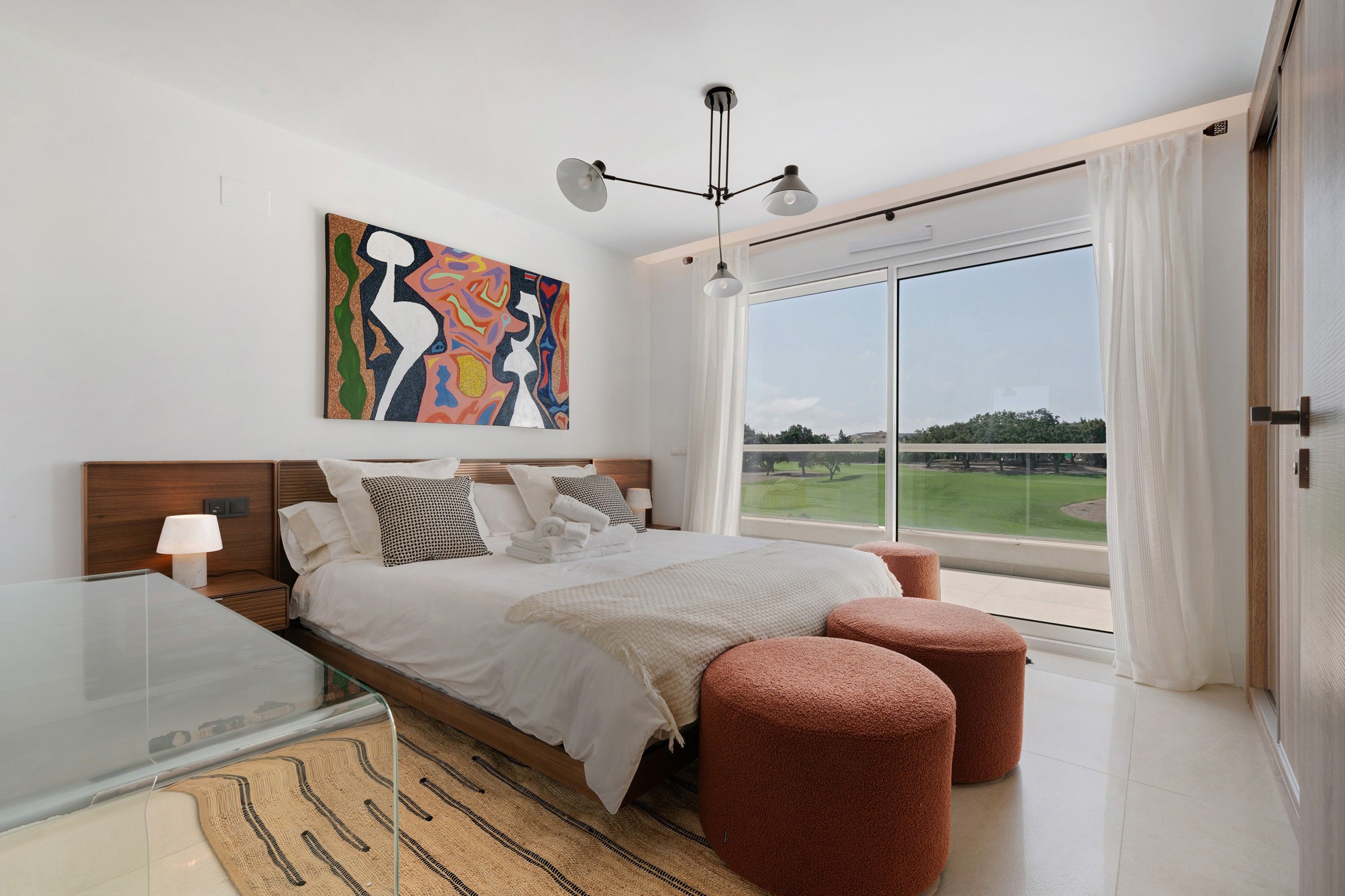 Un dormitorio moderno con una cama grande, vista a un campo de golf y un cuadro abstracto colorido.