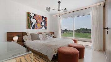 Un dormitorio moderno con una cama grande, vista a un campo de golf y un cuadro abstracto colorido.