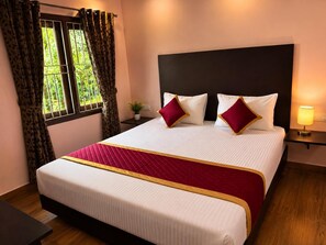Habitación de hotel con cama, cortinas, mesita de noche, lámpara y ventana con vistas a zonas verdes.