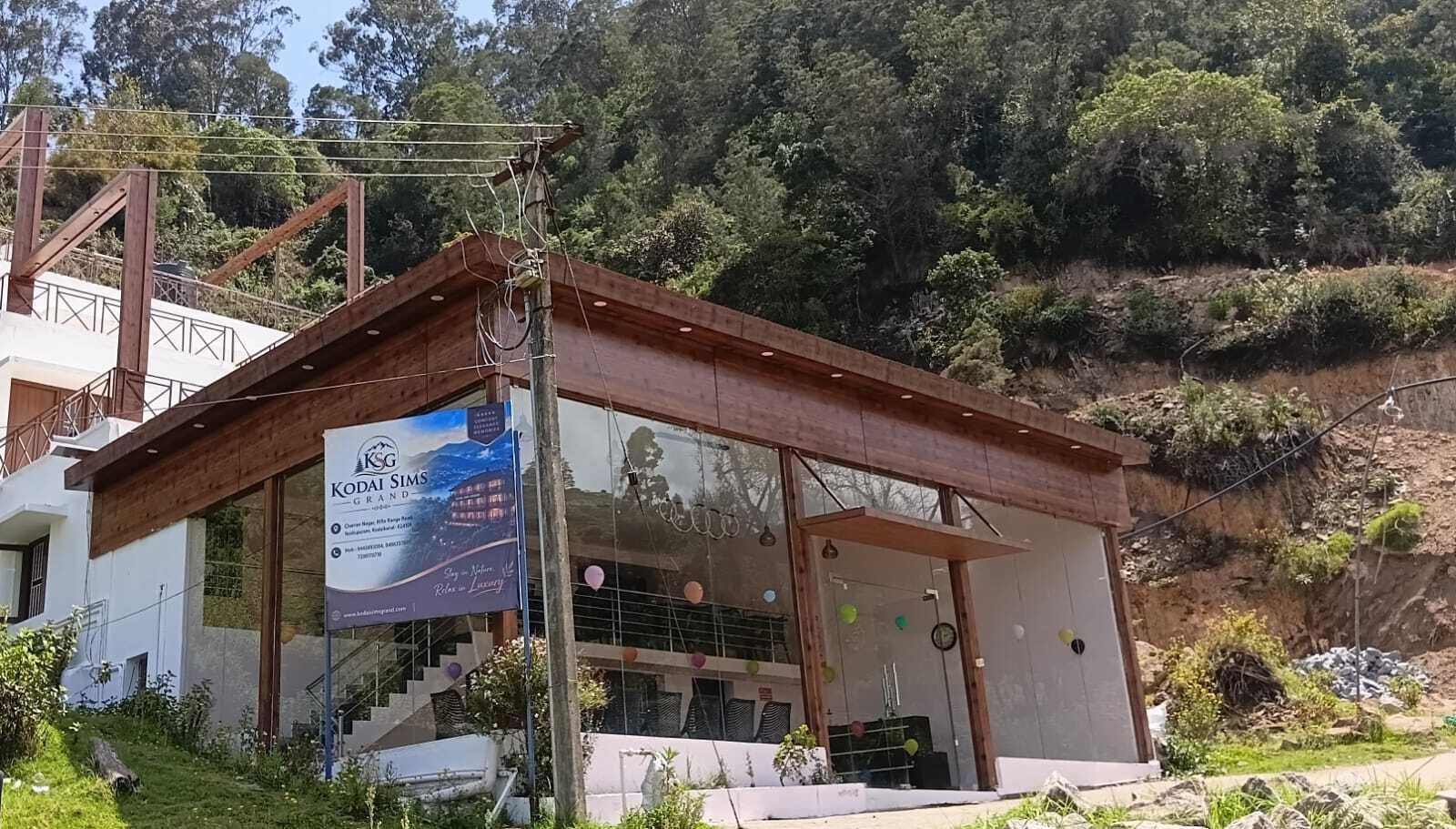 Un edificio con fachada de madera, un amplio ventanal y un letrero que anuncia KODAI SIMS GRAND.