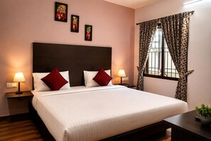 Una habitación de hotel con una cama grande, dos lámparas de noche, una mesita de noche, un ventanal con cortinas estampadas y cuadros en la pared.
