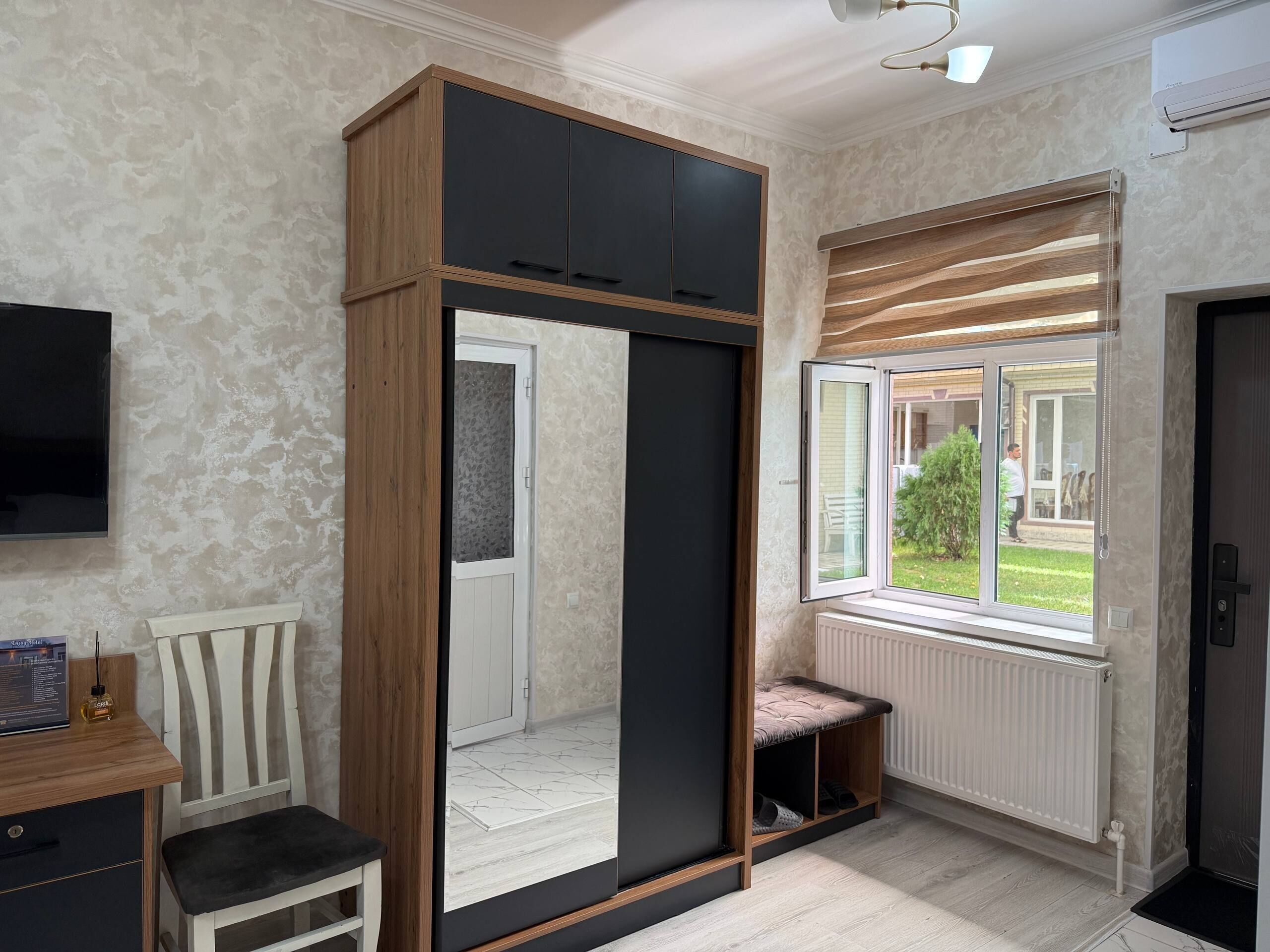 A room with a sliding wardrobe, a bench, a radiator, and a window with a view of the outside.