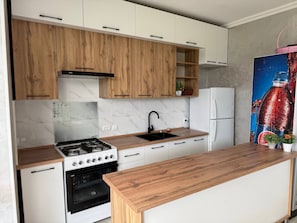 Una cocina moderna con armarios blancos, encimera de madera, estufa a gas y refrigerador.