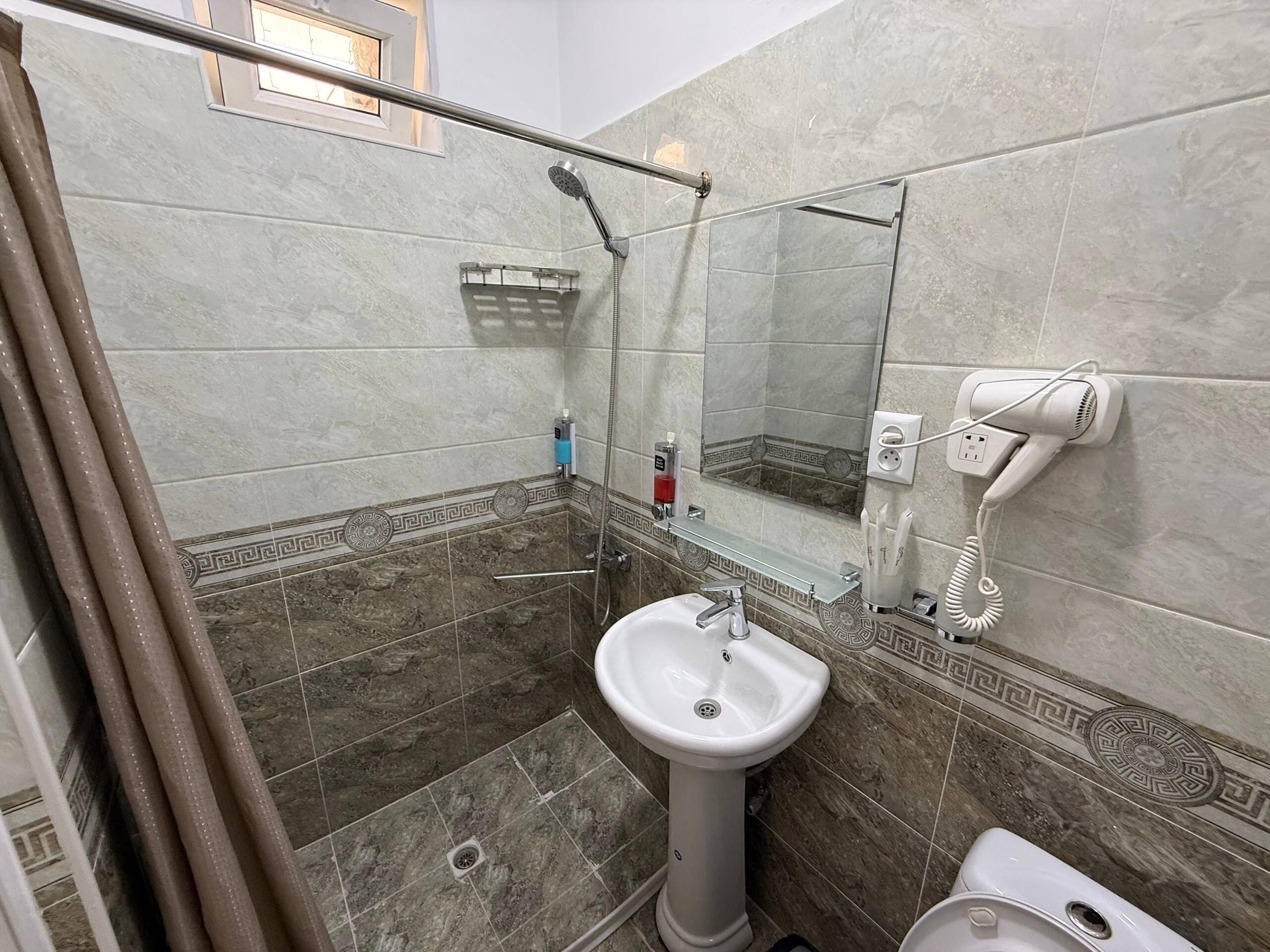 A bathroom with a shower, a sink, a toilet, and a hairdryer plugged in.