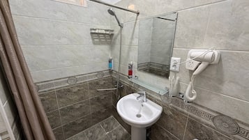 A bathroom with a shower, a sink, a toilet, and a hairdryer plugged in.