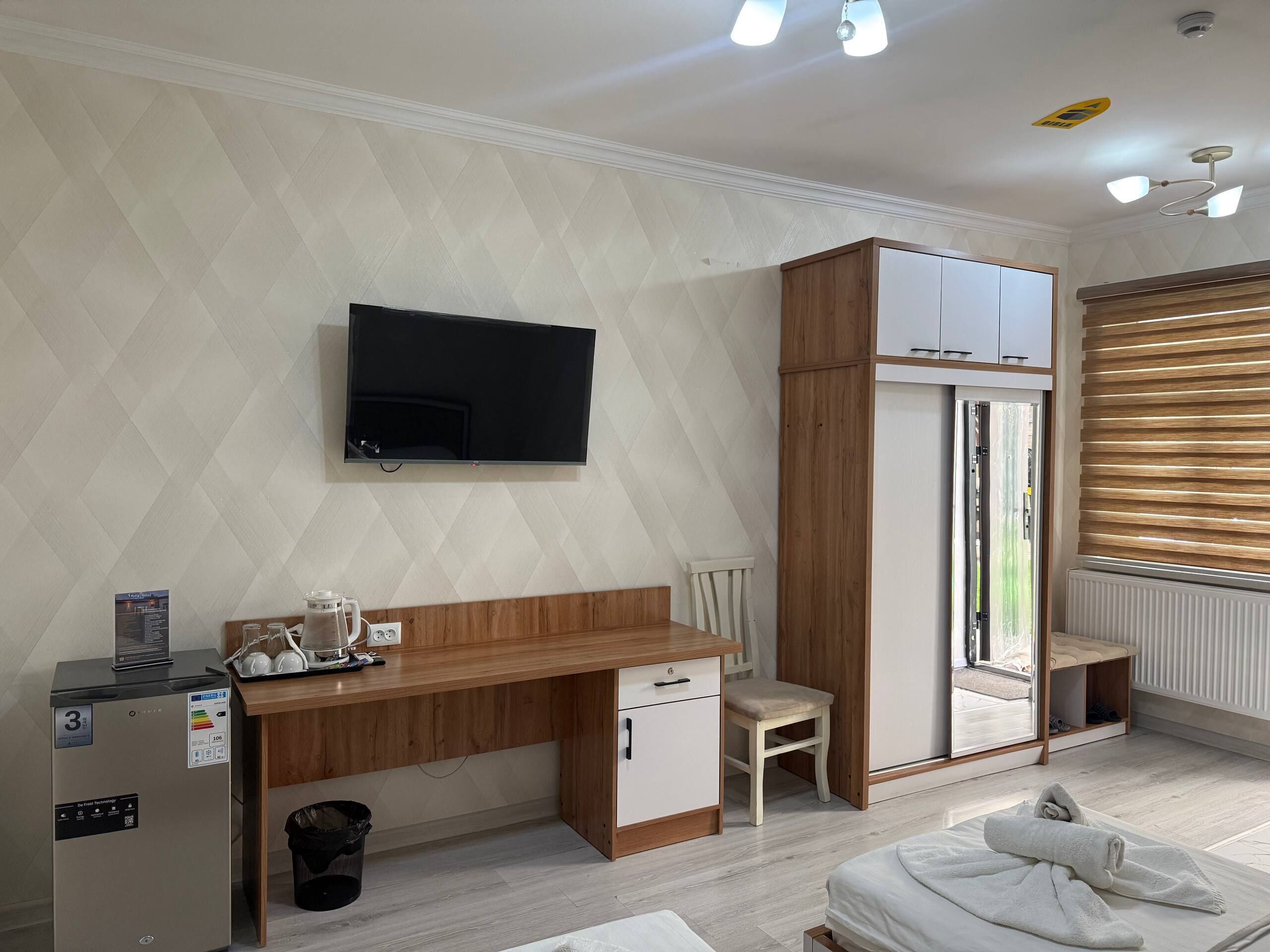 A bedroom with a bed, a desk with a chair, a television mounted on the wall, and a radiator.