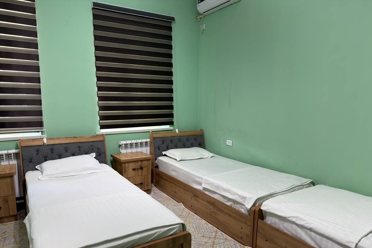 A room with three single beds, wooden headboards, and a radiator under the window blinds.
