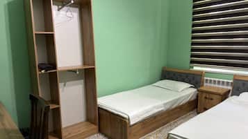Une chambre avec un lit simple, une armoire en bois, une table de chevet et une fenêtre avec des stores.