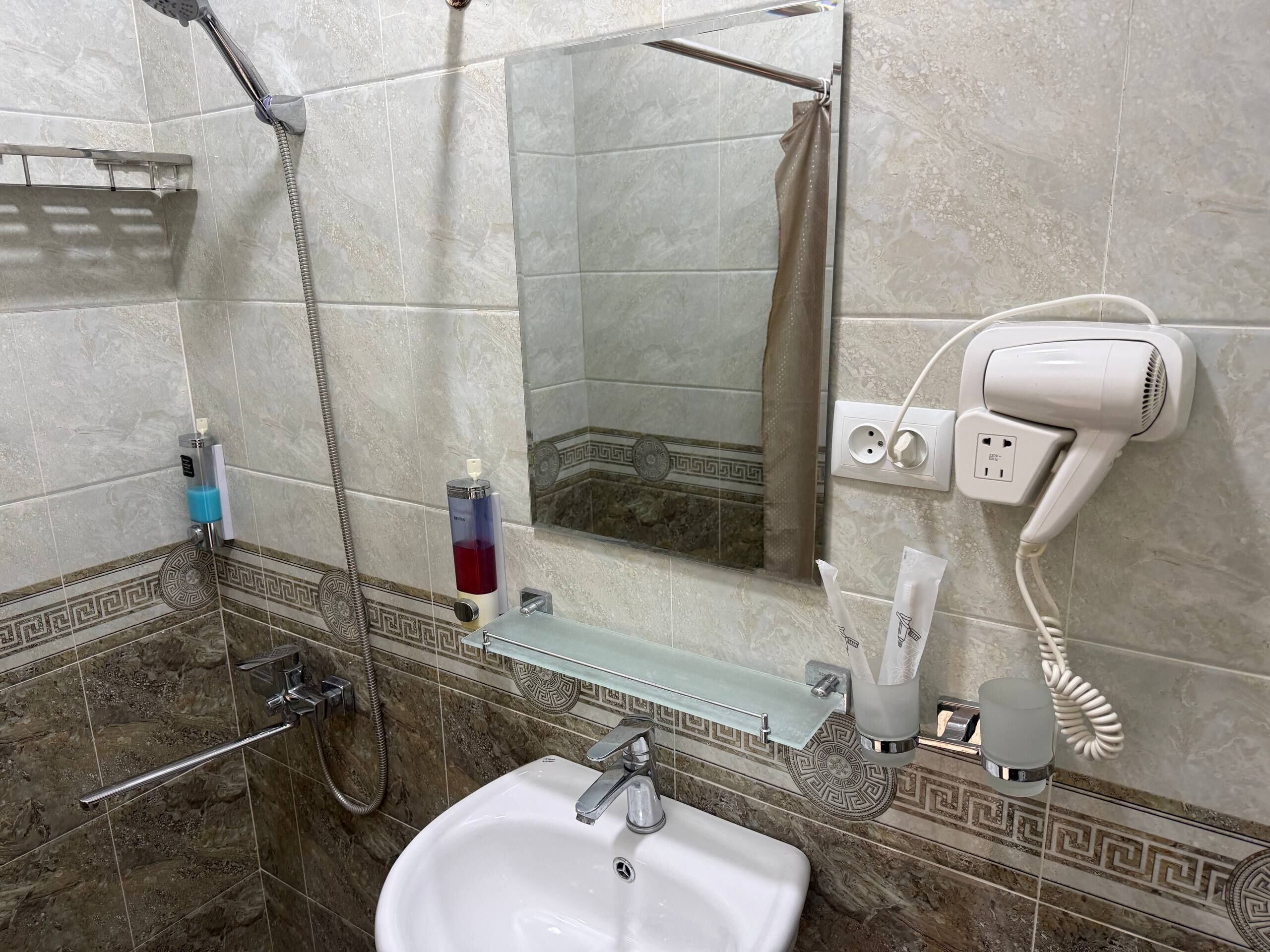 Une salle de bain équipée d’un lavabo, d’un miroir, d’une douche et d’un sèche-cheveux.
