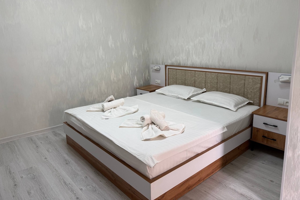 A neatly made bed with white linens and towels, a wooden headboard, and a bedside table with a lamp.