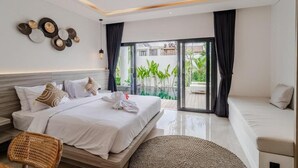 A modern bedroom with a bed, a sofa, a rattan chair, a woven rug, and a view of greenery through a sliding glass door. - Majys 4 Villa by Tasvan (Badung)