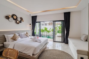 Een moderne slaapkamer met een bed, een bank, een rieten stoel, een geweven vloerkleed en uitzicht op groen via een schuifdeur.