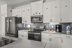 A modern kitchen with stainless steel appliances, white cabinetry, and decorative magnets. - 4BR Disney Getaway | Pool, Pirate & Castle Rooms (Davenport)