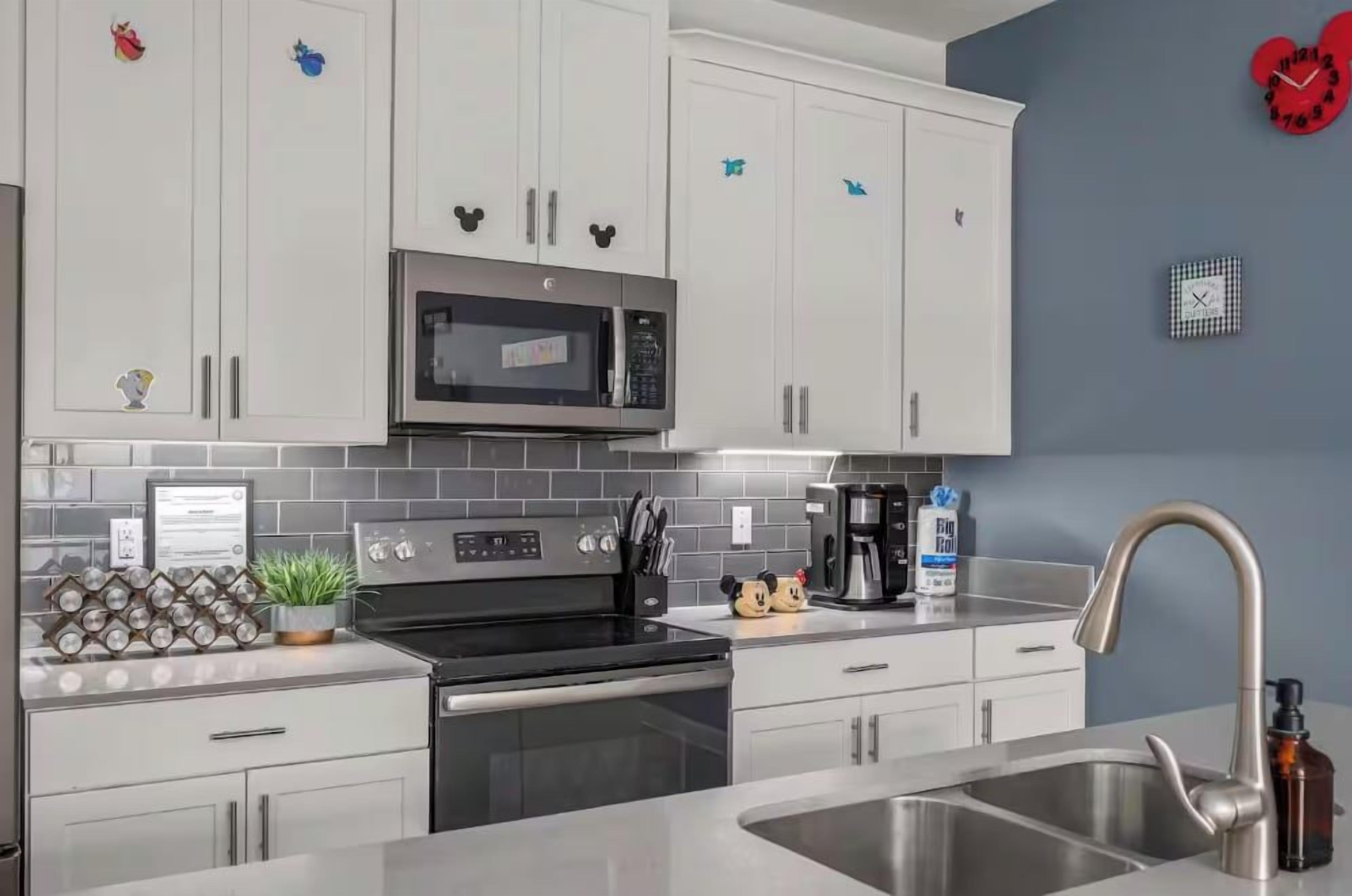 Una cocina moderna con armarios blancos, un microondas de acero inoxidable y una cafetera.