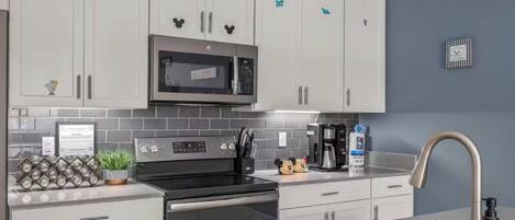 Una cocina moderna con armarios blancos, un microondas de acero inoxidable y una cafetera.