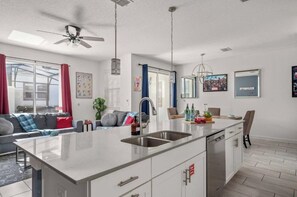 A modern kitchen with a central island, a dining area with a sofa, and a ceiling fan. - 4BR Disney Getaway | Pool, Pirate & Castle Rooms (Davenport)