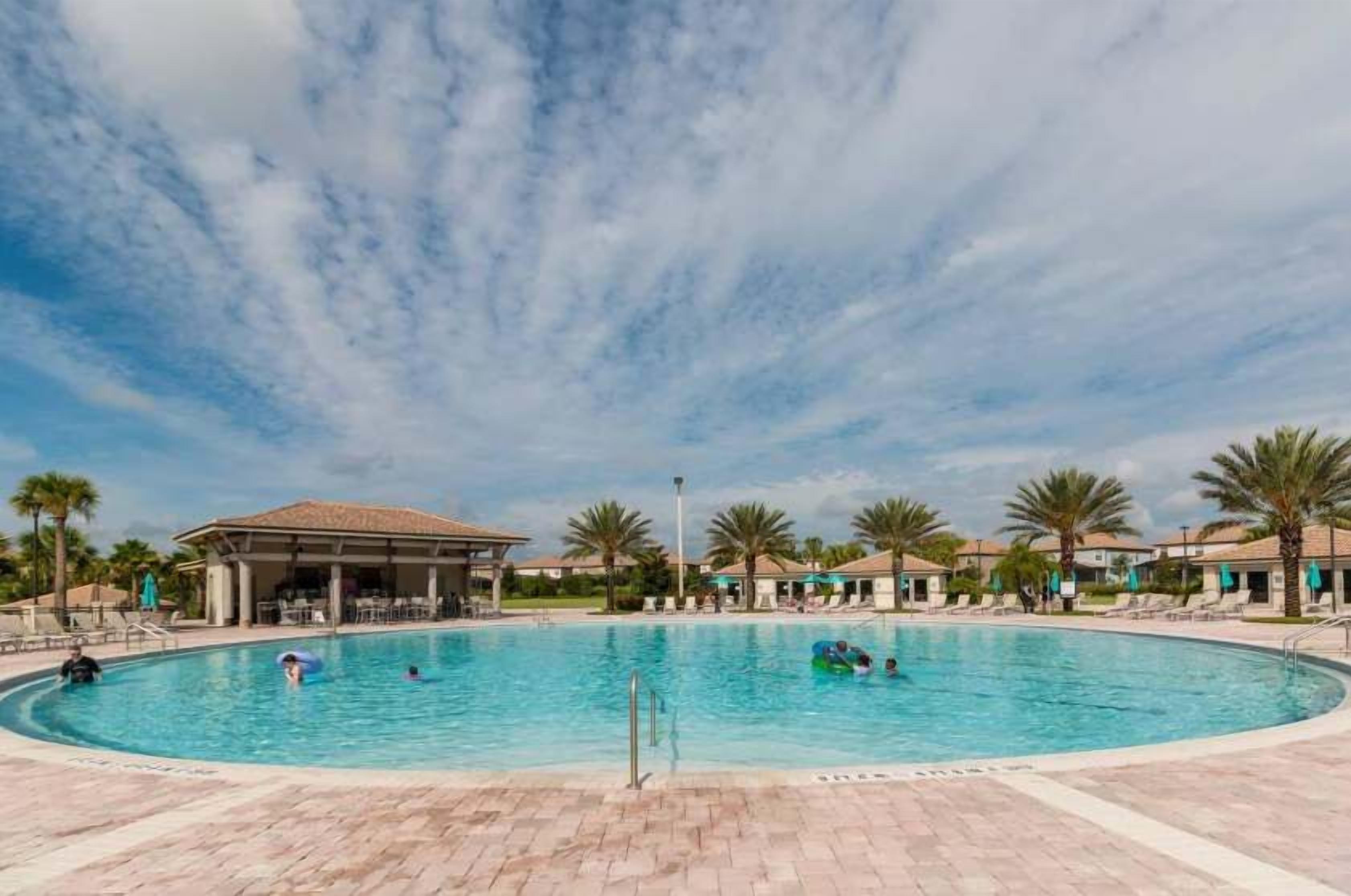 Una gran piscina al aire libre con un pabellón cubierto, palmeras y cielo despejado.
