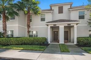 A two-story residential building with a front entrance, palm trees, and a well-maintained lawn. - 4BR Disney Getaway | Pool, Pirate & Castle Rooms (Davenport)