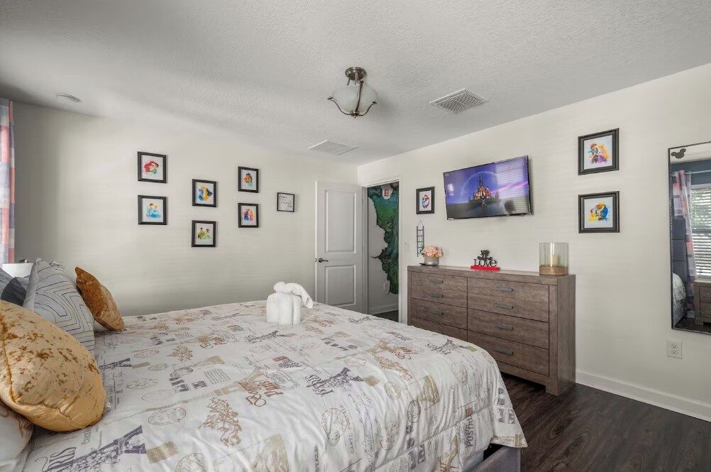 A bedroom with a bed, dresser, and wall-mounted TV.