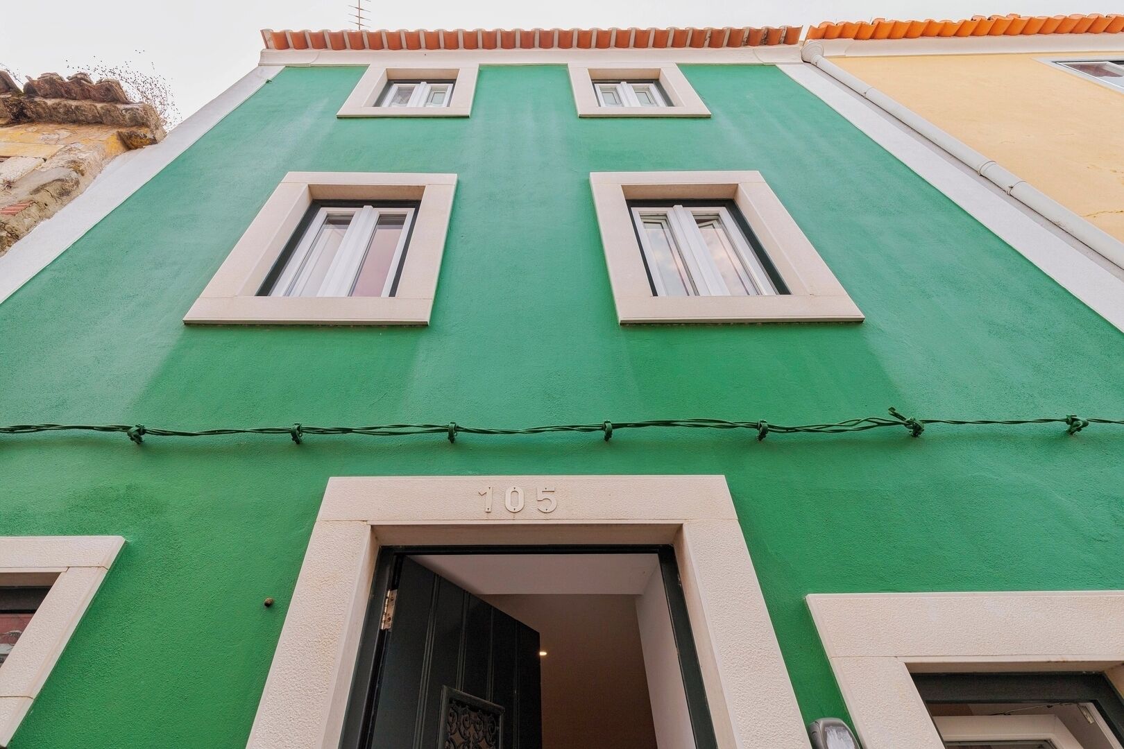 A building with a green facade, numbered 105, featuring multiple windows and a visible entrance.
