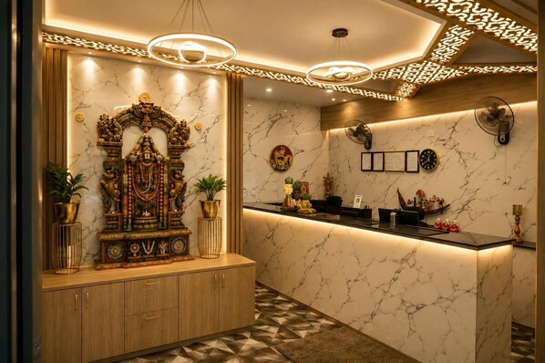 A reception area with a marble wall, a decorative statue, a reception desk, and a patterned floor.