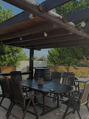 Eine Außenpatio mit Holztisch und Stühlen, einem Grill und einer Pergola darüber.