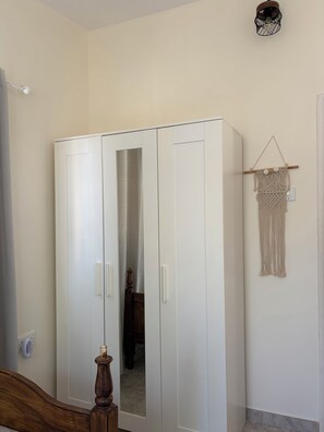 A room with a white wardrobe, a wooden bed frame, and a macrame wall hanging. - Terra Olive Hideaway 3 bedroom villa (Pegeia)