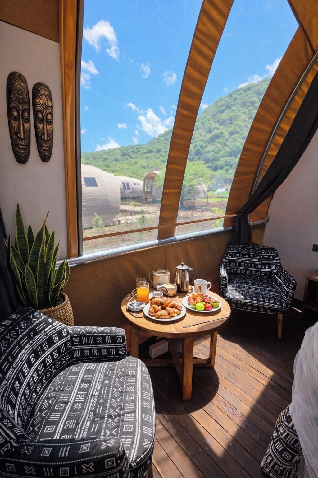 Un comedor con una mesa dispuesta para el desayuno, una planta en maceta y vista a un tren por la ventana.