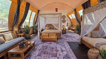 A tented accommodation with a central bed, two sofas, a dining area, and a view of the outdoors.