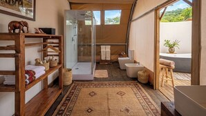 A modern bathroom with a glass shower, a bathtub, and a toilet. There is a wooden shelf with towels and a hanging rack. - Africa Safari Manyara Migombani (mto wa mbu)