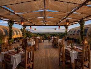 An outdoor dining area with tables and chairs, covered by a canopy, and surrounded by greenery. - Africa Safari Manyara Migombani (Lake Manyara National Park)