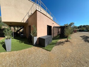 A modern building with a flat roof, a covered outdoor area with artificial grass, and a gravel path.