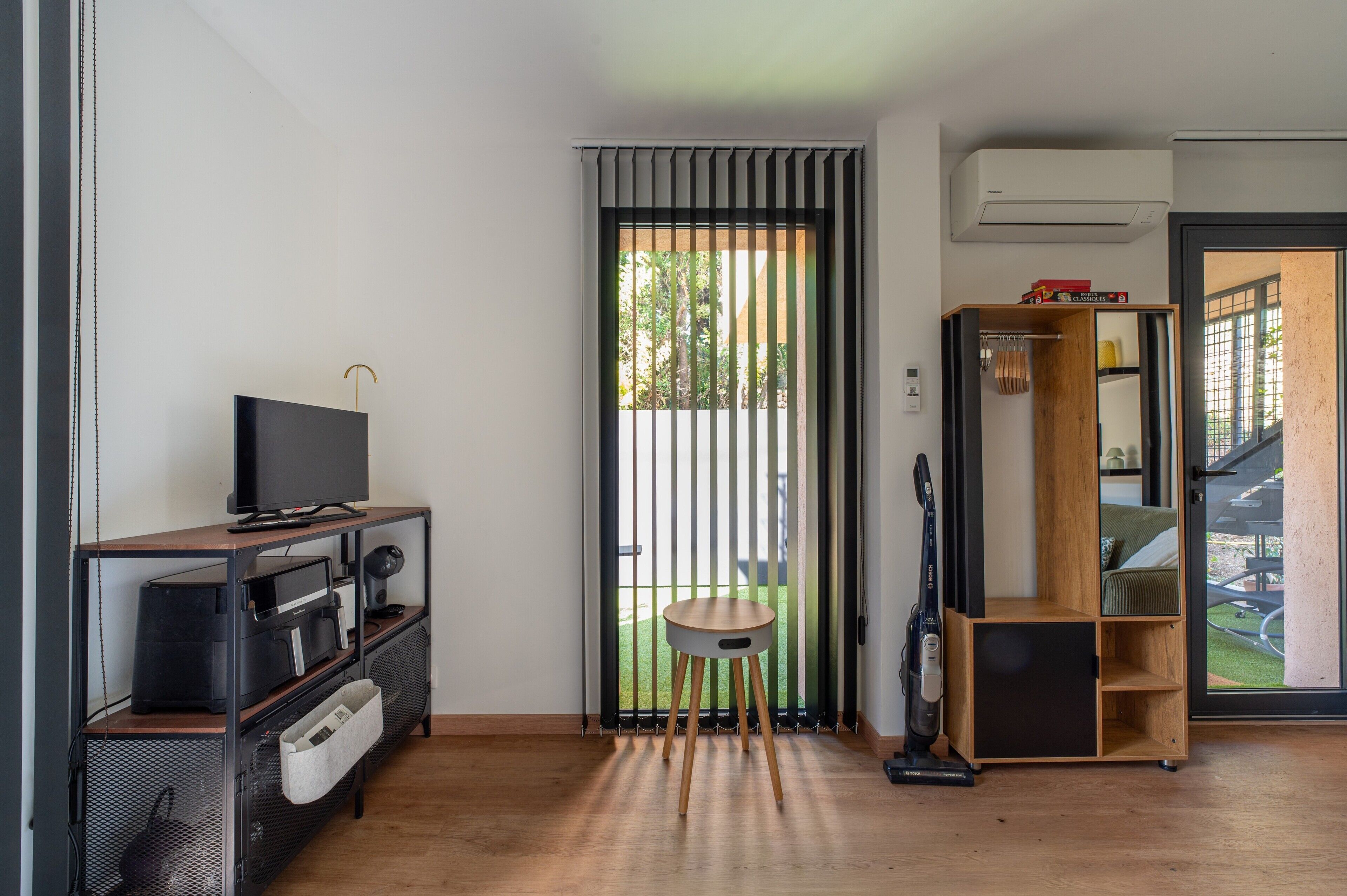 A modern living room with a flat-screen TV, a vacuum cleaner, and a wooden cabinet.