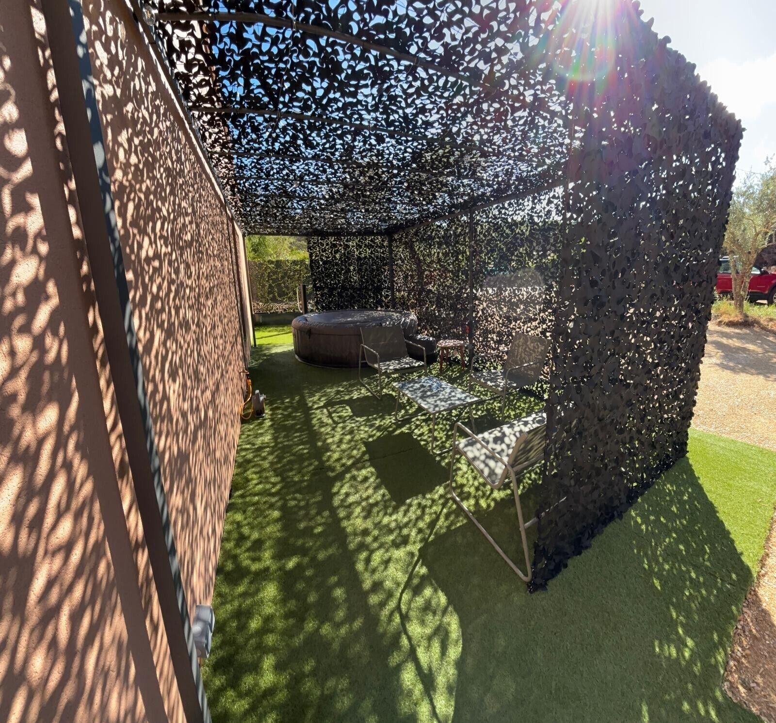 Un espacio de descanso al aire libre cubierto, con jacuzzi y sillas, rodeado por una cerca decorativa.