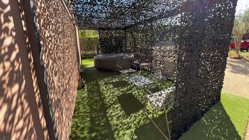 Un espacio de descanso al aire libre cubierto, con jacuzzi y sillas, rodeado por una cerca decorativa.
